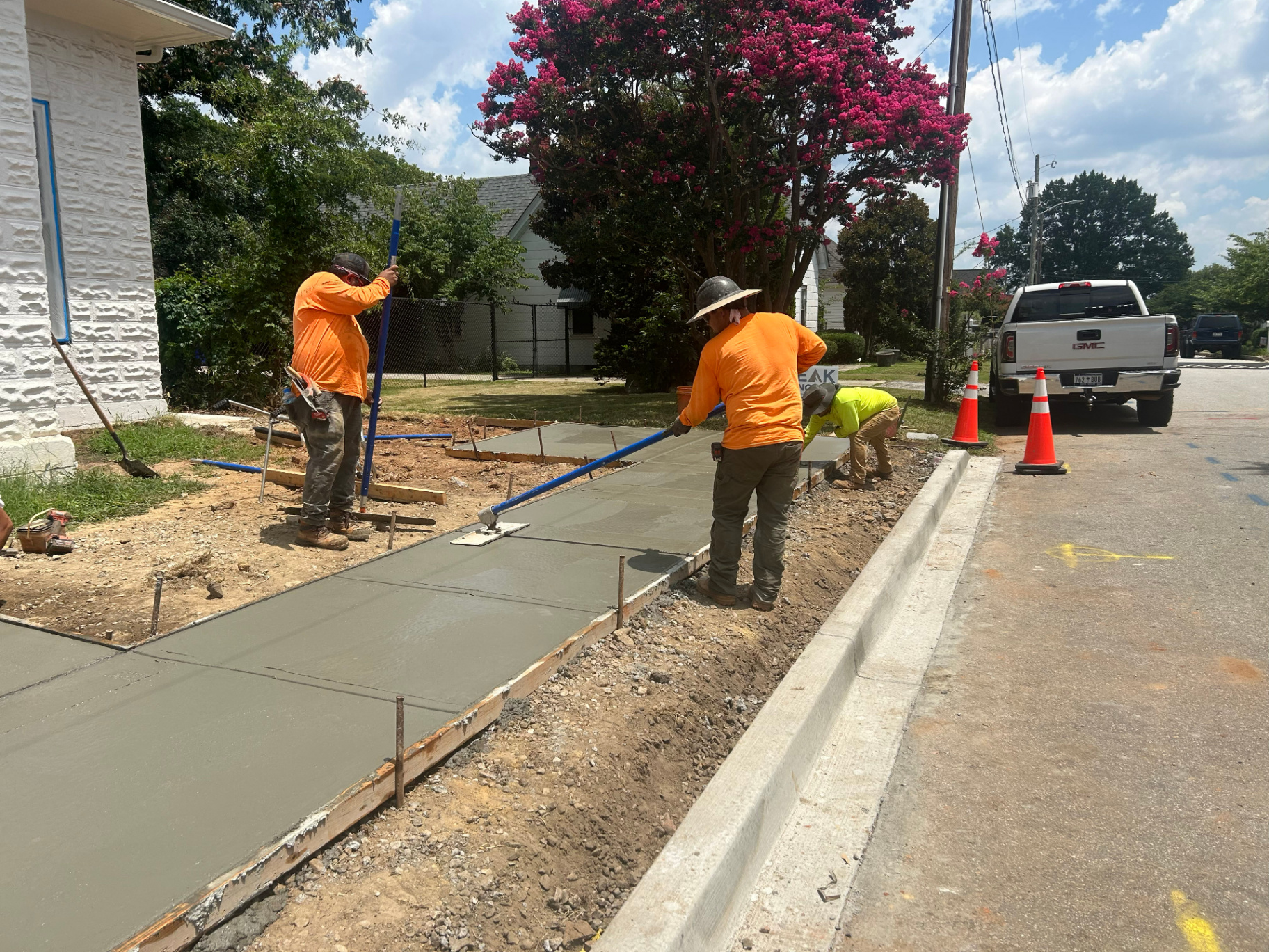 Peak Concrete finishers using a bull float and edger to smooth a curbside sidewalk pour along a residential street.