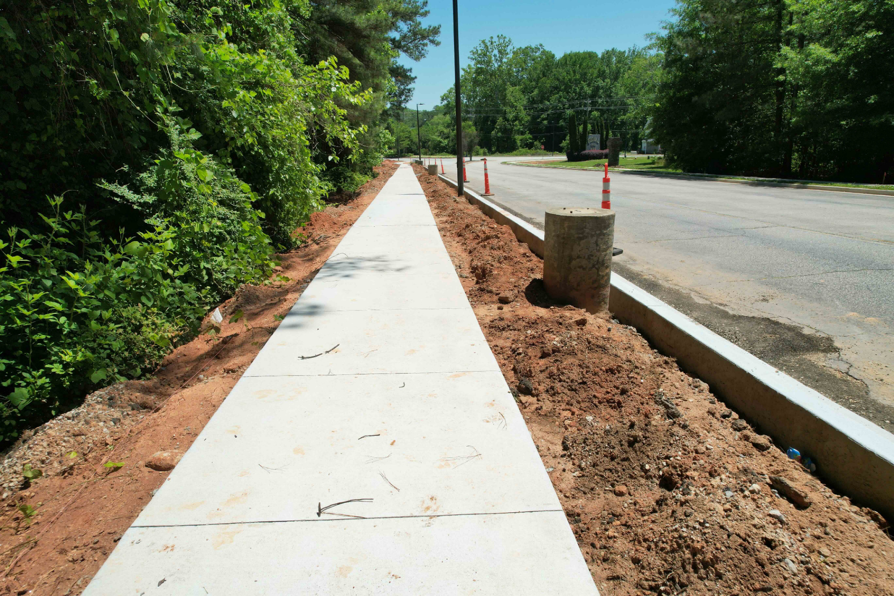 Long straight run of finished concrete sidewalk and curb along Global Drive, tied into asphalt roadway with dirt backfill on both sides.