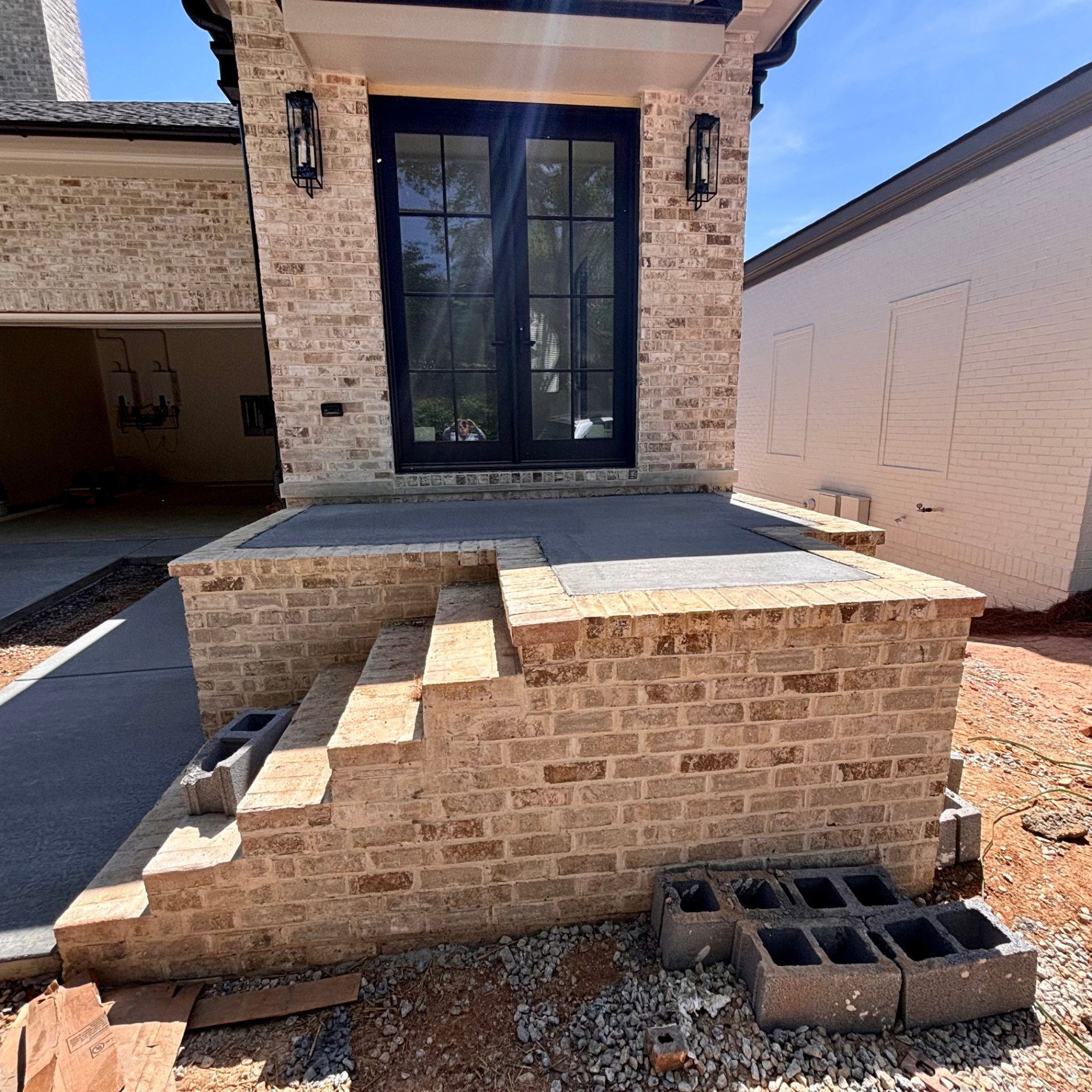 Freshly poured concrete stoop landing at the front door of a new custom brick home, framed by a brick knee wall with brick step treads leading down to the driveway.