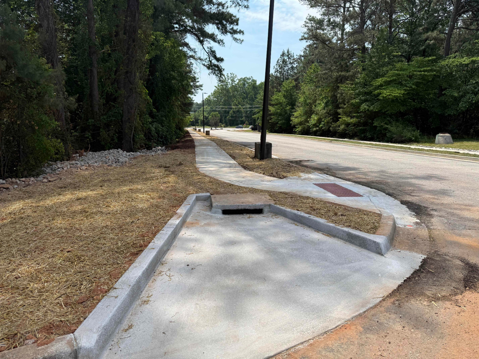 Completed ADA curb ramp and valley gutter at a street corner with detectable warning pad, sidewalk transitioning into the intersection.