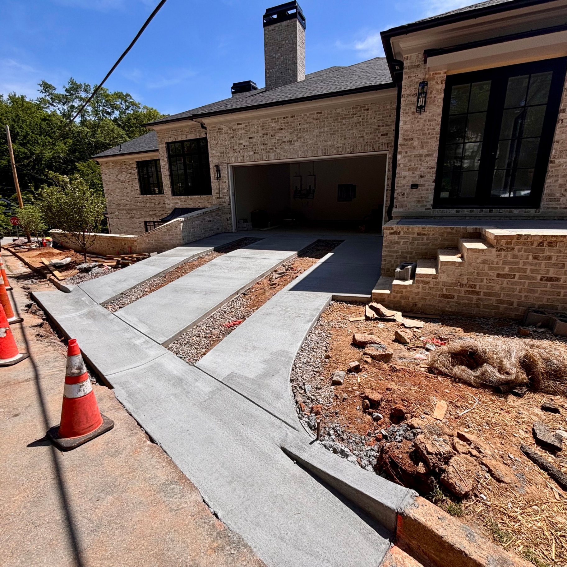 New broom-finished concrete driveway with ribbon strips and gravel infill leading to the garage of a custom brick home, curved apron tying into the street.